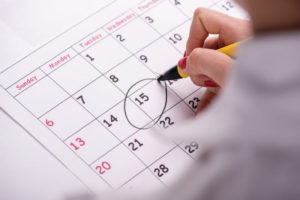 Close-up top-view photo of calendar with a datum circled by young woman with red nails with a back marker, concept of time management at work