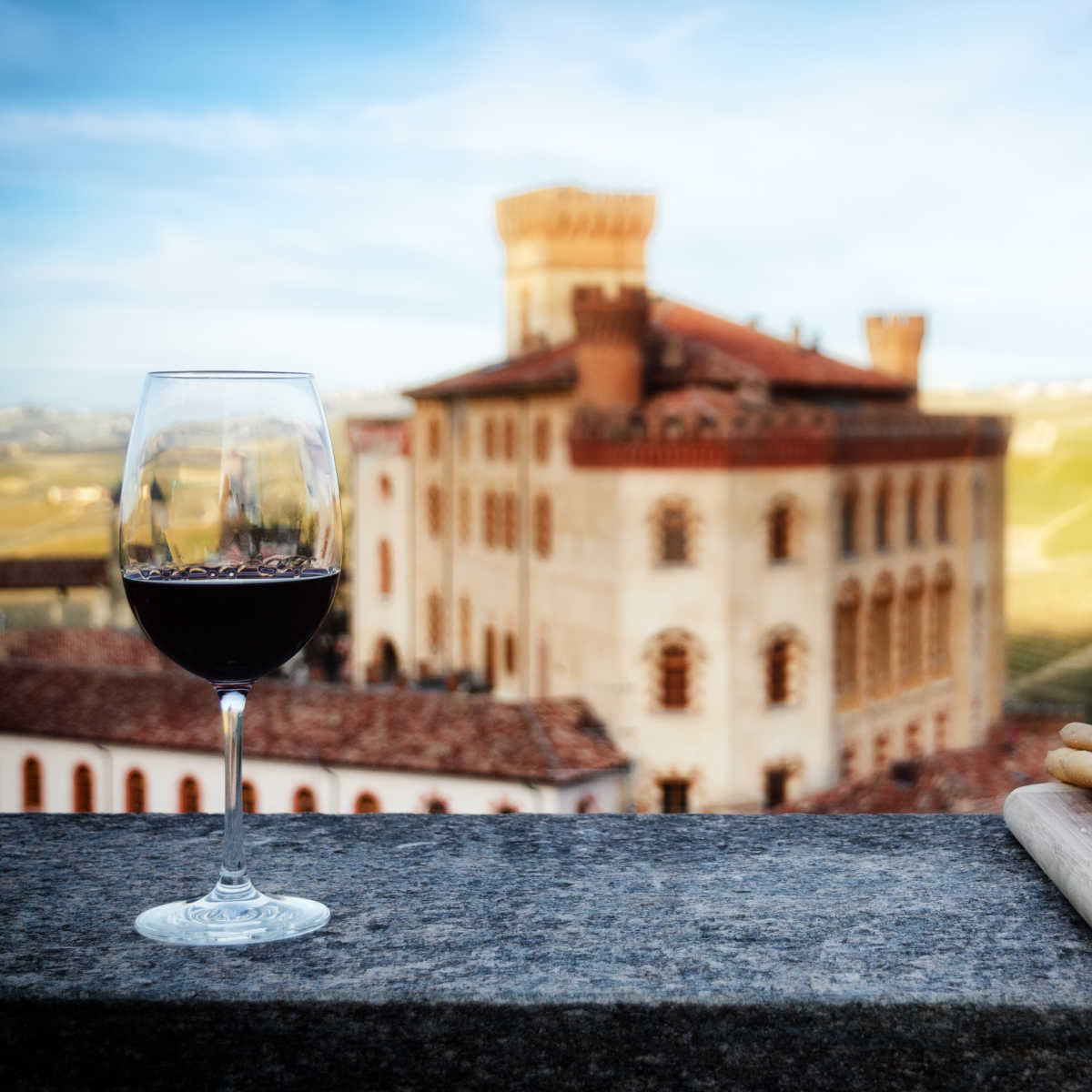 A chalice of Barolo red wine on a windowsill with breadsticks and the castle of Barolo (Piedmont, Italy) on the background